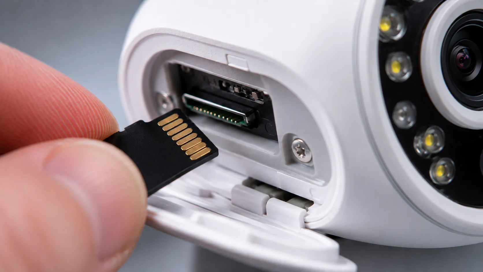 Fingers inserting a microSD card into the card slot of a white security camera for local recording