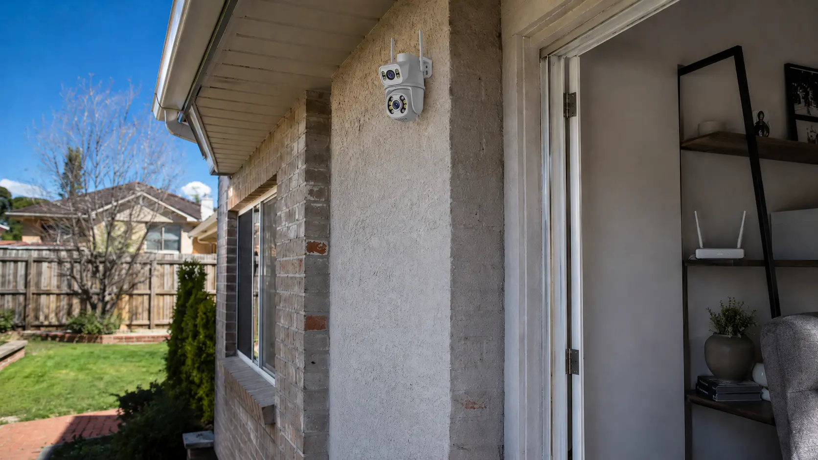 White outdoor WiFi security camera mounted high on a house wall, far from a WiFi router visible indoors through the doorway
