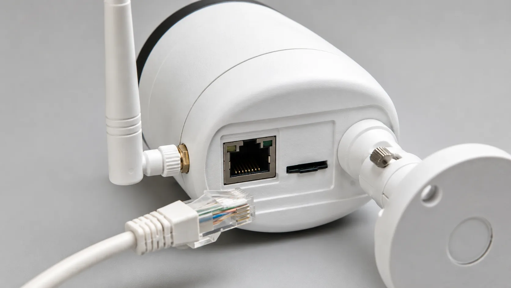 Close-up of a white outdoor camera showing its external antenna, RJ45 wired-backup port with cable, and microSD card slot